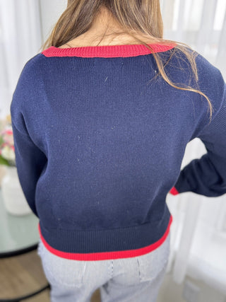 Person wearing a navy sweater with red trim, standing indoors.