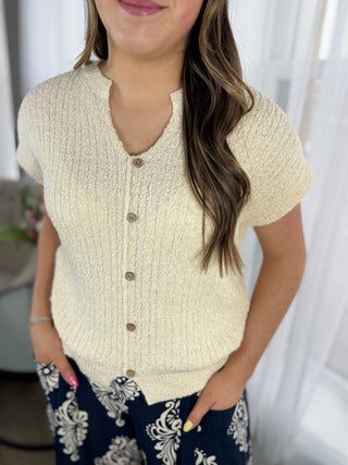 Woman wearing a textured cream cardigan over a patterned outfit with a blurred background