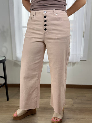 Person wearing beige pants with button details in a room with white curtains.