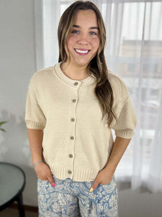 Woman wearing a beige cardigan with a blurred indoor background