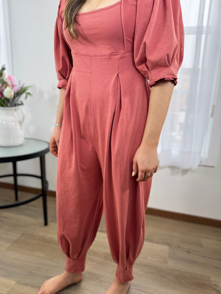 Person wearing a pink jumpsuit standing indoors with a blurred background