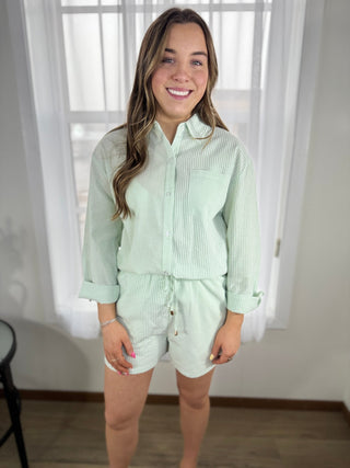 Woman wearing a light green checkered shirt and shorts set indoors.