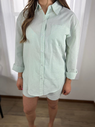 Person wearing a light green and white striped shirt with rolled-up sleeves against a neutral background