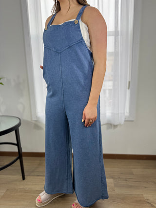 Person wearing blue denim overalls standing indoors with a neutral background