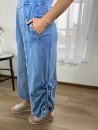 Person wearing blue denim pants standing indoors with a neutral background
