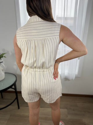 Woman wearing a beige and white striped romper in a room with white curtains.