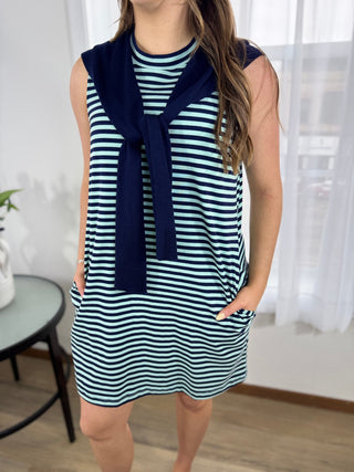 Woman wearing a navy and white striped dress with a navy scarf in a room with white curtains.