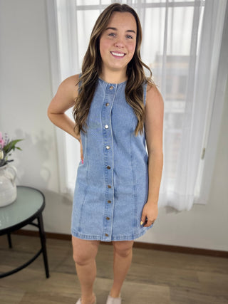 Woman wearing a denim dress standing in a room with white curtains.