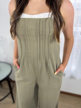 Person wearing a green jumpsuit with a white top underneath, standing indoors.