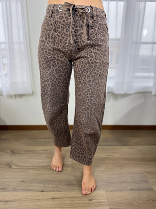 Leopard print pants worn by a person on a wooden floor with white curtains in the background