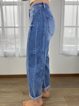 Person wearing blue jeans standing in a room with wooden flooring and white curtains.