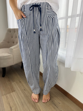 Person wearing navy and white striped pajama pants in a room with a chair and window.