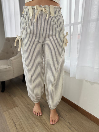 Striped pants worn by a person in a room with curtains and a chair.