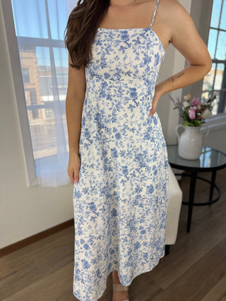 Woman wearing a blue and white floral dress in a room with a window and table.