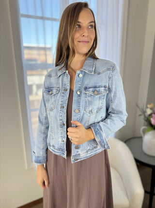 Woman wearing a light blue denim jacket indoors with a blurred background