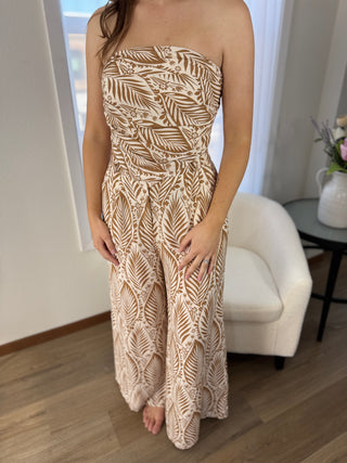 Woman wearing a strapless dress with a leaf pattern in a room with a white chair and table.
