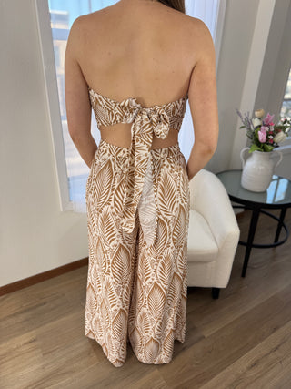 Person wearing a strapless, patterned jumpsuit in a room with a window and furniture.