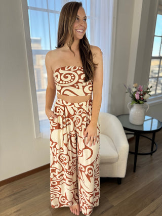 Woman wearing a strapless top and wide-leg pants with a pattern in a room with large windows.