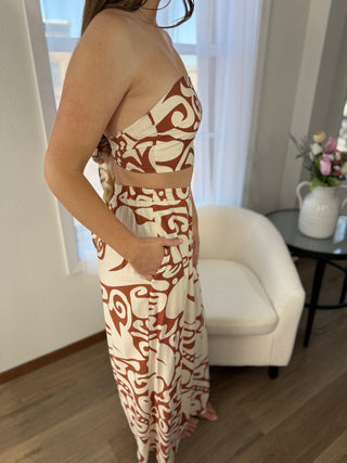 Person wearing a strapless dress with a geometric pattern in a room with a white armchair and a table with flowers.