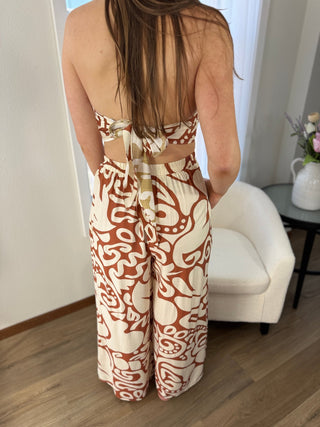 Person wearing a patterned outfit standing in a room with a white chair and table.