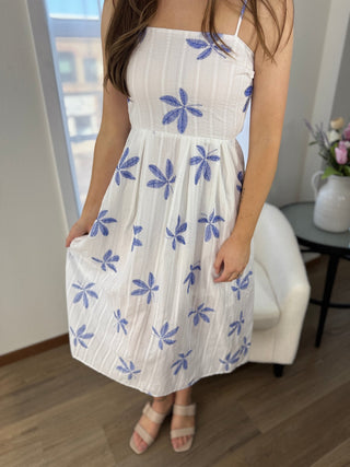 Woman wearing a white dress with blue floral patterns indoors.