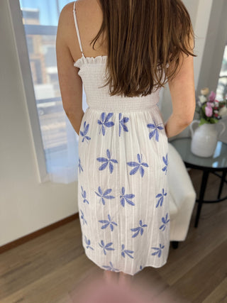 Woman wearing a white dress with blue floral patterns indoors.