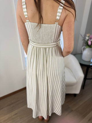 Person wearing a striped dress in a room with a white wall and a small table with a vase.