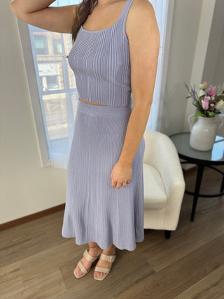Woman wearing a light purple striped dress in a room with a white chair and a small table with a vase.