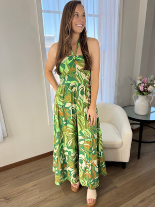 Woman wearing a green patterned dress standing in a room with a couch and table.