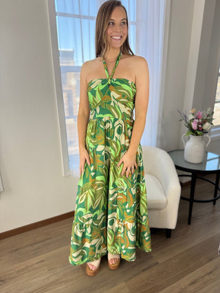 Woman wearing a green and yellow floral dress standing in a room with a window and furniture.