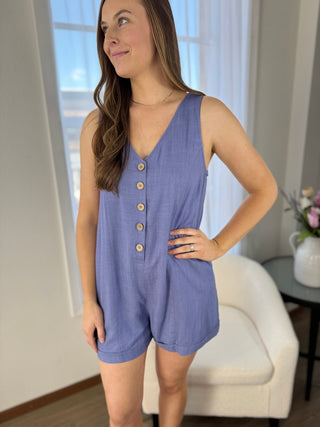 Woman wearing a blue romper in a room with a window and chair.
