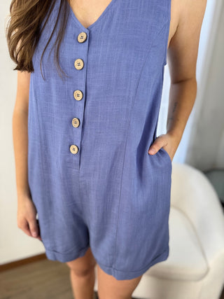 Person wearing a blue romper with buttons in a minimal indoor setting