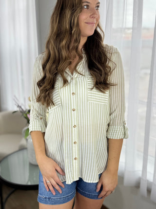 Woman wearing a striped shirt and denim shorts in a bright room with sheer curtains.