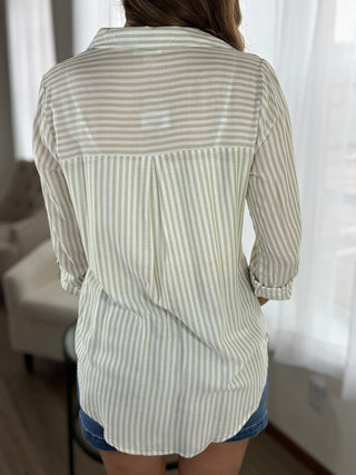 Person wearing a green and white striped shirt in a room with curtains.