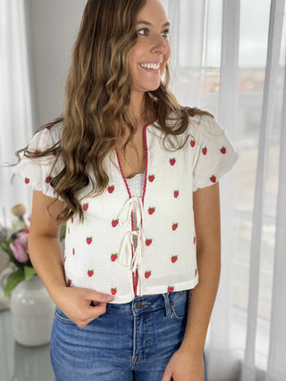 Woman wearing a white blouse with red patterns and blue jeans indoors.
