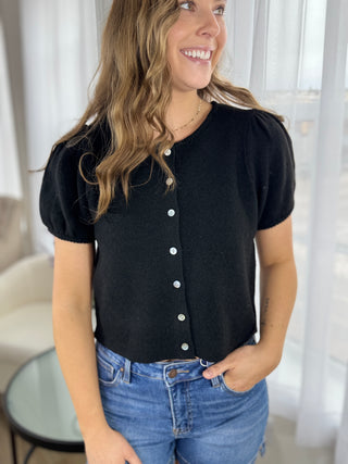 Woman wearing a black button-up shirt and blue jeans indoors.