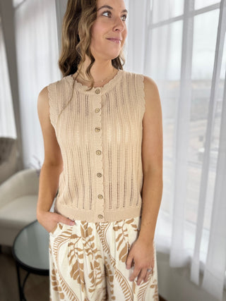 Woman wearing a beige sleeveless knitted cardigan in a bright room.