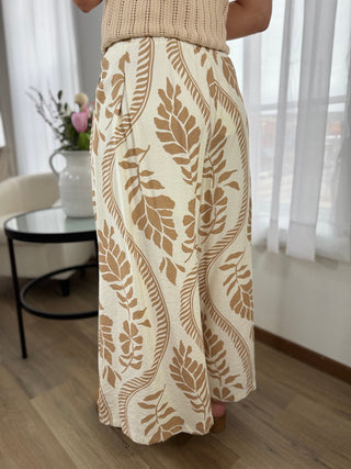 Person wearing a beige patterned skirt in a room with light curtains and a table.