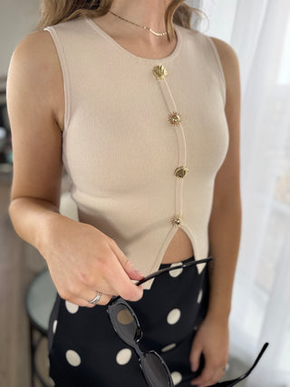 Beige sleeveless top with decorative buttons worn by a person, holding sunglasses.