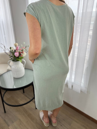 Person wearing a light green dress standing in a room with a table and flowers in the background.
