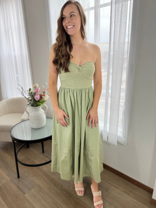 Woman in a light green dress standing in a room with a table and flowers.