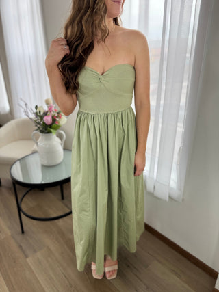 Woman wearing a green strapless dress in a room with white curtains and a small table with flowers.