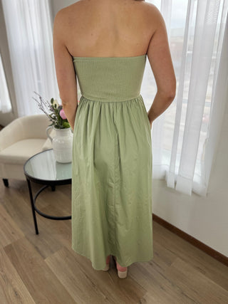 Person wearing a strapless green dress in a room with white curtains and a glass table.