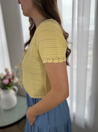Woman wearing a yellow crochet top with a blurred background
