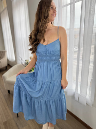 Woman wearing a blue dress in a bright room with large windows.