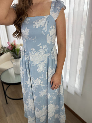 Woman wearing a blue floral dress indoors with a blurred background