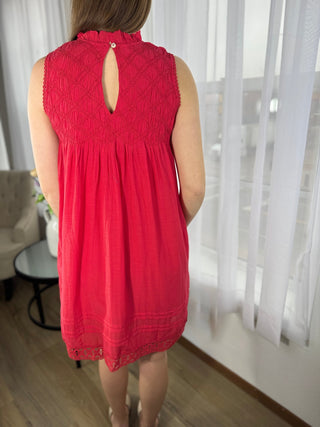 Person wearing a red sleeveless dress in a room with white curtains.
