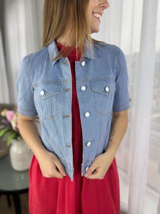 Woman wearing a blue denim jacket over a red dress indoors.