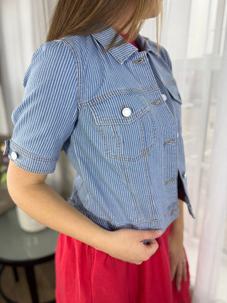 Person wearing a blue striped denim jacket over a red dress indoors.