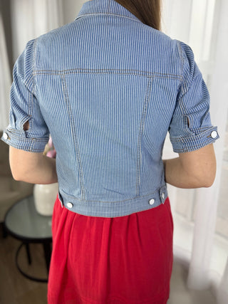 Person wearing a blue striped shirt with rolled-up sleeves and red pants in a neutral setting